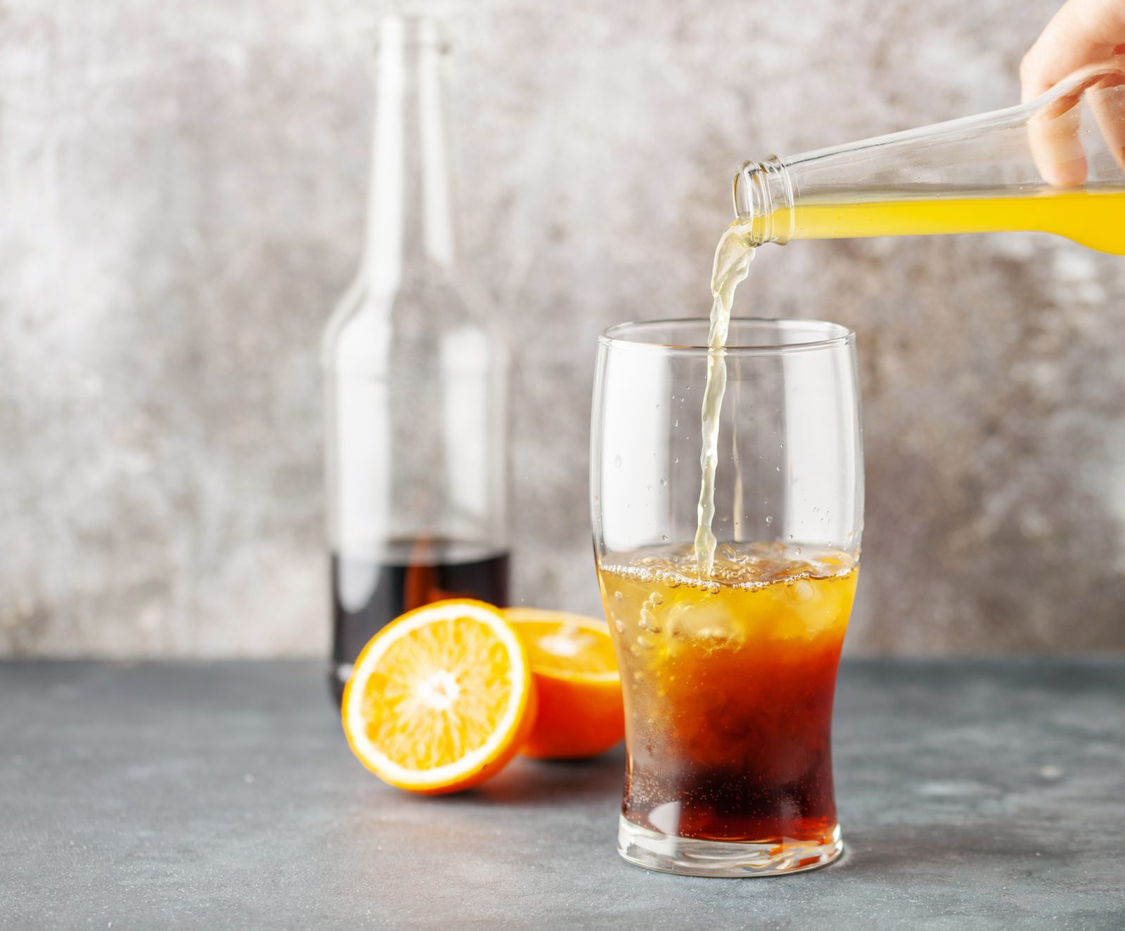 In einem Glas, das bereits Cola enthält, wird Limonade aus einer Flasche hinzugefügt
